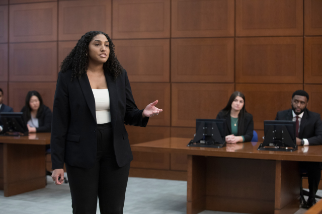 A woman in a black suit stands in a courtroom speaking